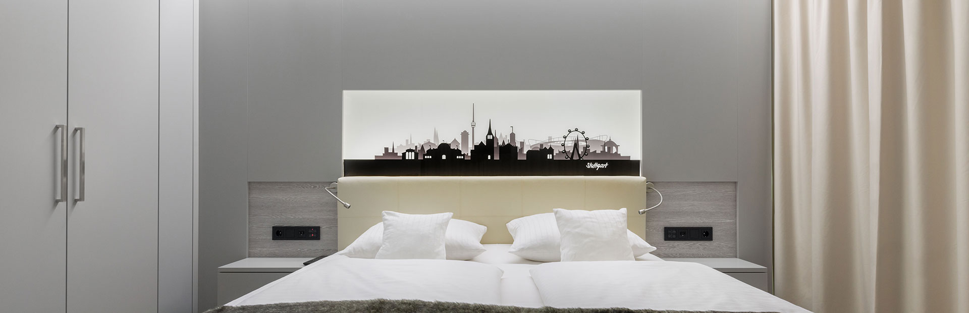 Luxuriöses Schlafzimmer mit beleuchteter Silhouette von Stuttgart im SI-SUITES Hotel Stuttgart.