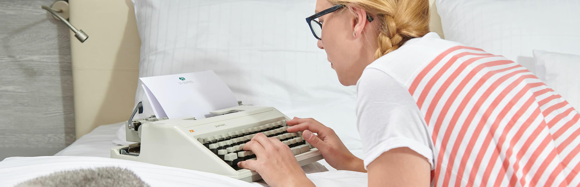 Frau arbeitet auf dem Bett mit Schreibmaschine in den SI-SUITES